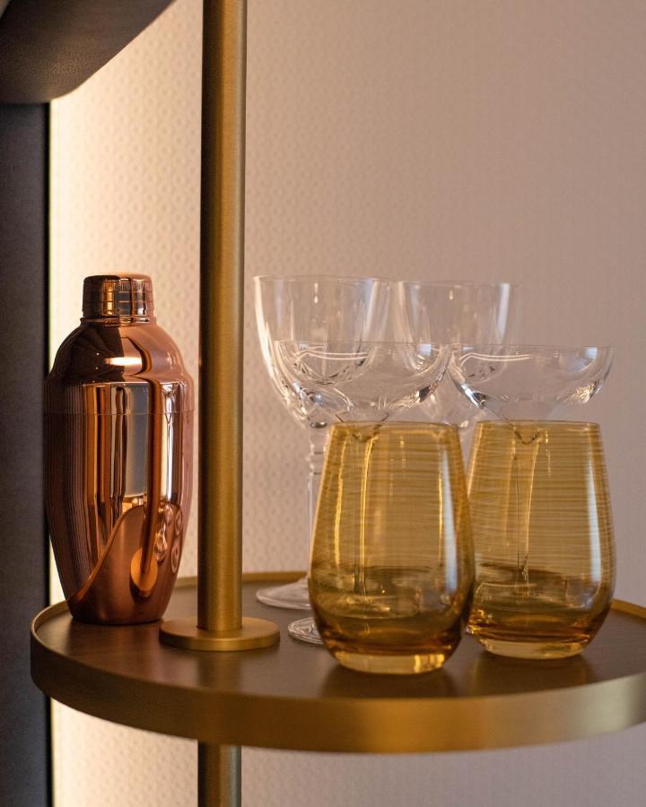 Middle Eight - Covent Garden - Preferred Hotels And Resorts London Kültér fotó The photo shows a stylish bar setup featuring a shiny copper cocktail shaker positioned next to several elegant glassware pieces. There are four tall, clear stemmed glasses and two round, amber-colored glasses with a textured pattern. The background 