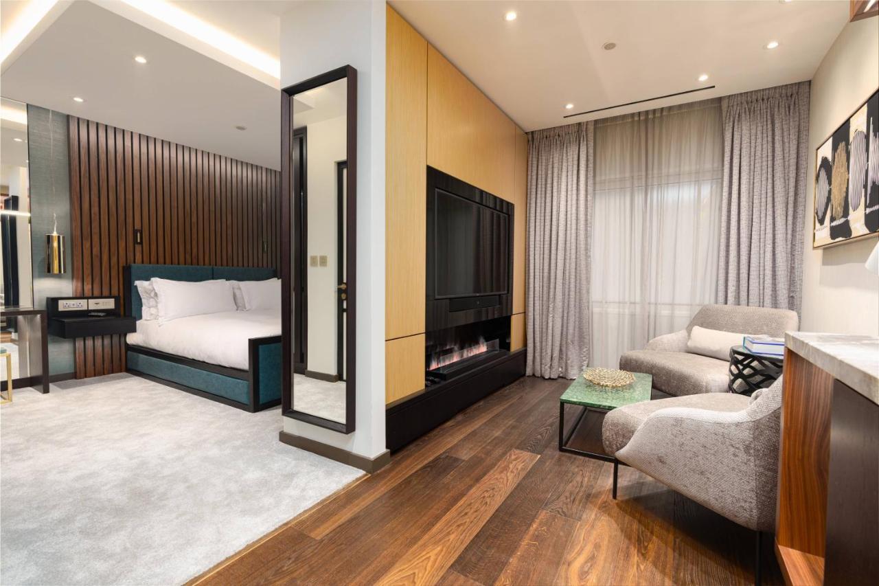 Middle Eight - Covent Garden - Preferred Hotels And Resorts London Kültér fotó The photo depicts a modern hotel room or suite featuring a cozy living space. On one side, there's a comfortable bed with plush bedding, positioned against a backdrop of elegant wooden paneling. Adjacent to the bed is a contemporary fireplace integra